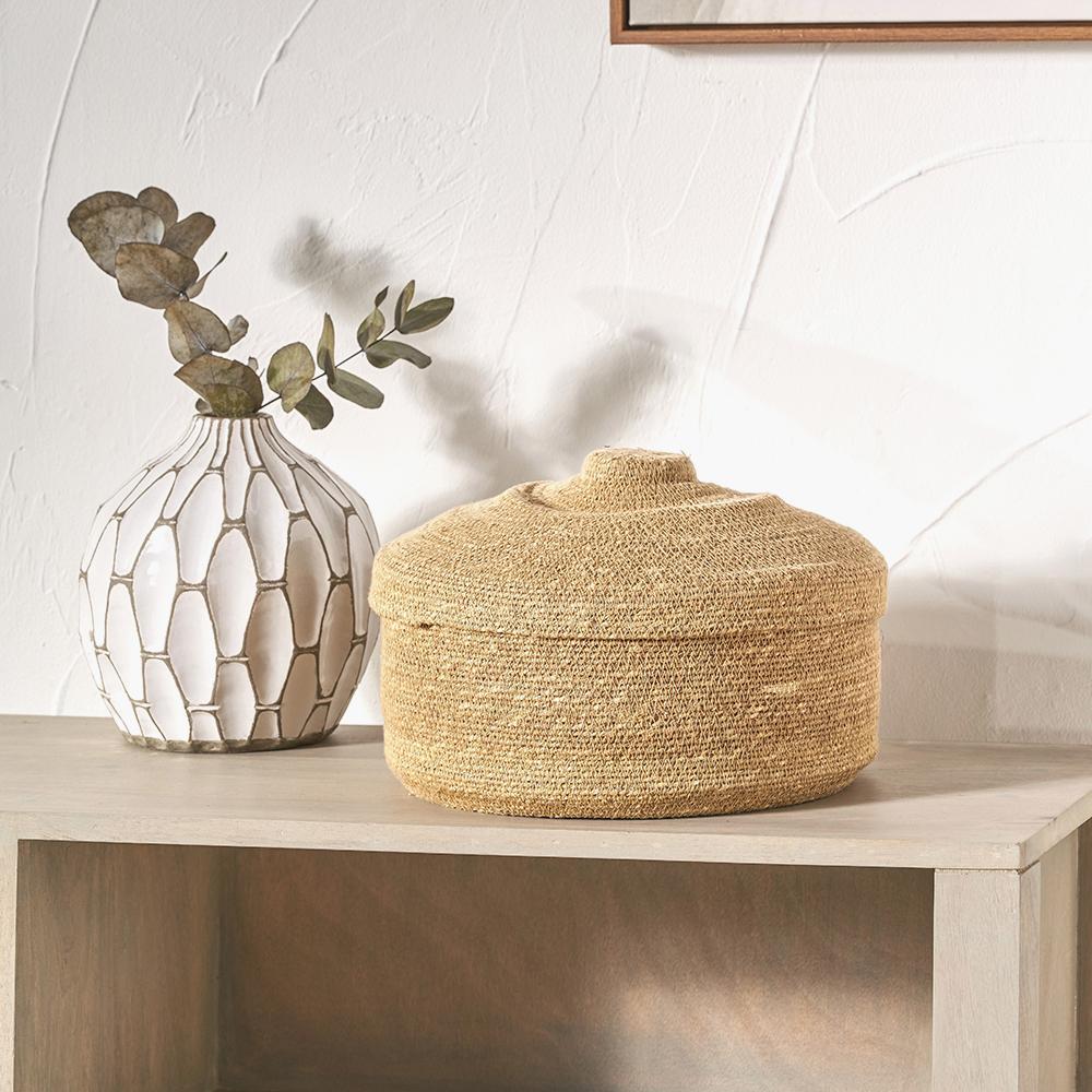A textured vase, a woven basket and eucalyptus styled on a console.