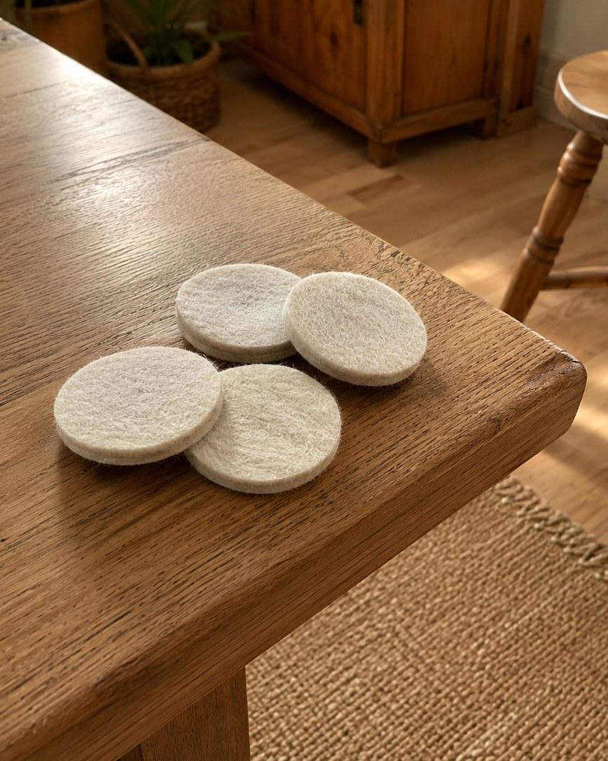Four round wool felt pads resting on the corner of a waxed oak dining table