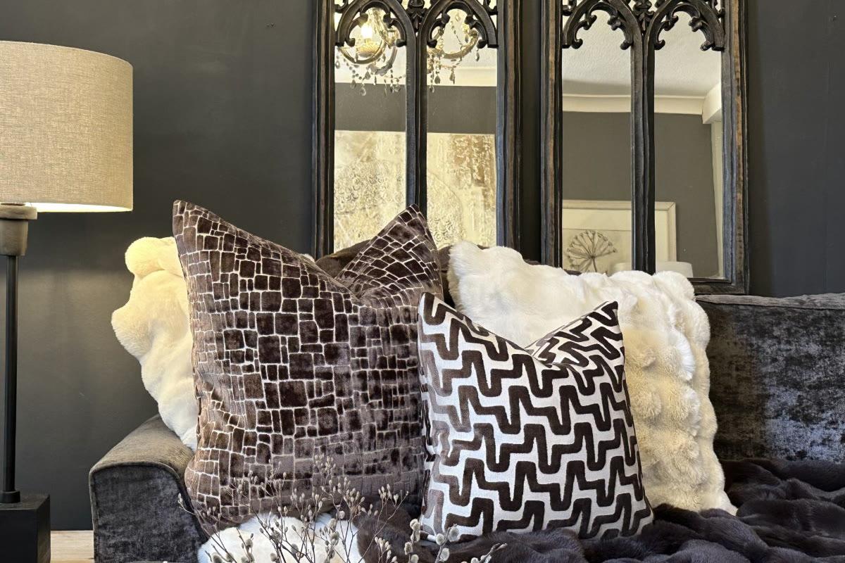 Malini chocolate velvet cushions and a cream faux-fur throw beneath a pair of arched fretwork mirrors