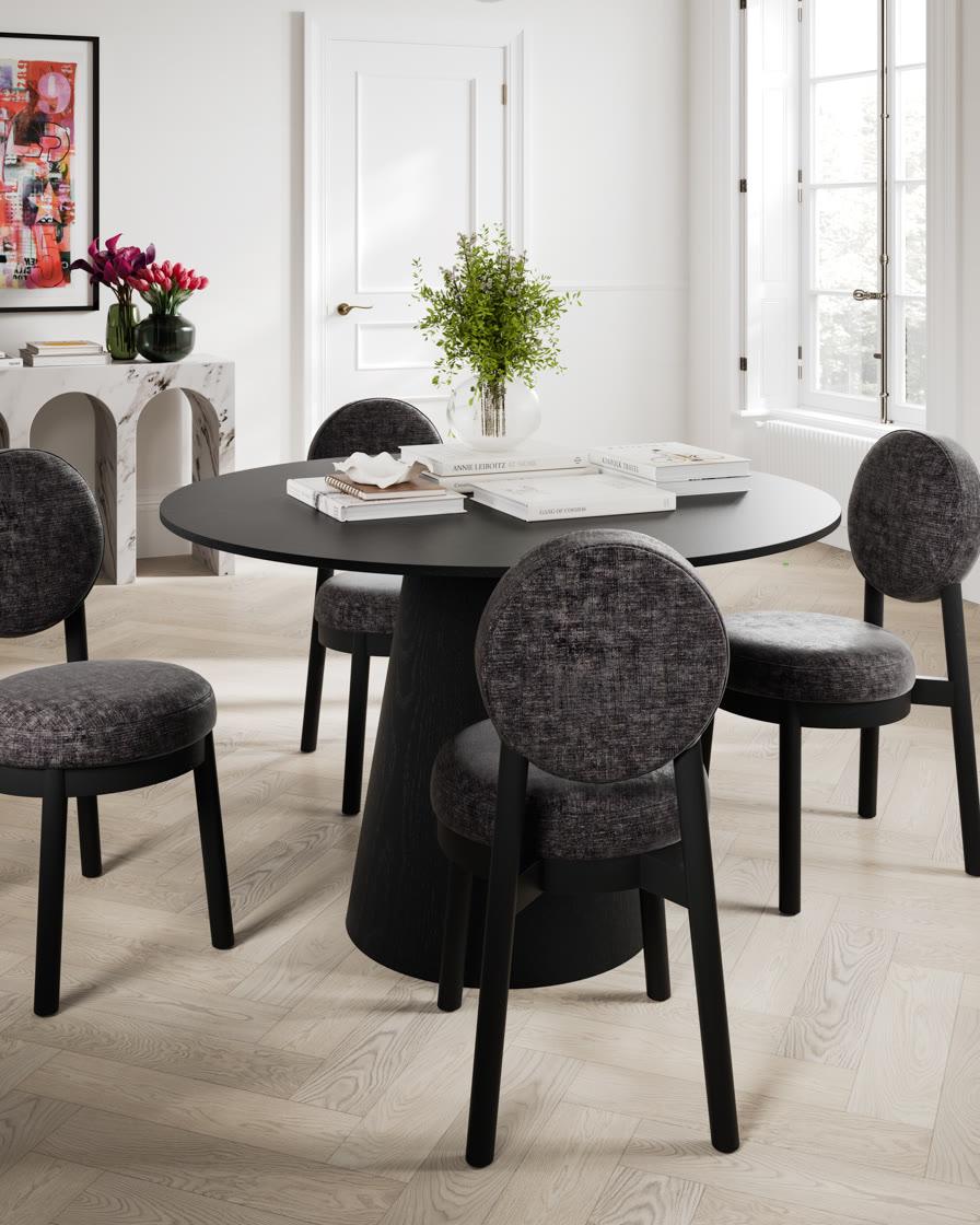 An LPD Maru round black dining table with four grey upholstered chairs on herringbone oak