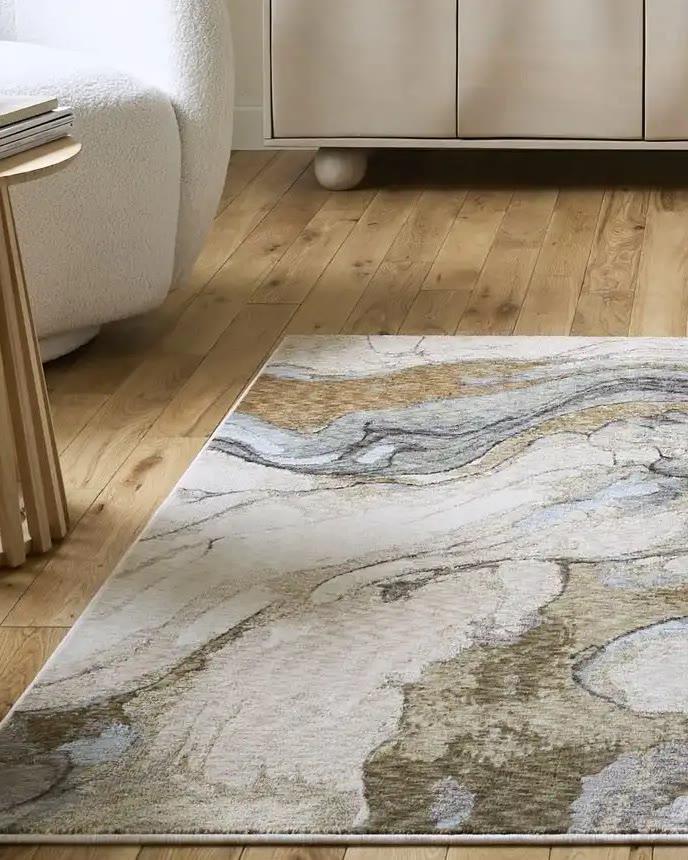 A Think Rugs marbled rug in gold and grey on oak boards, beside a cream bouclé chair