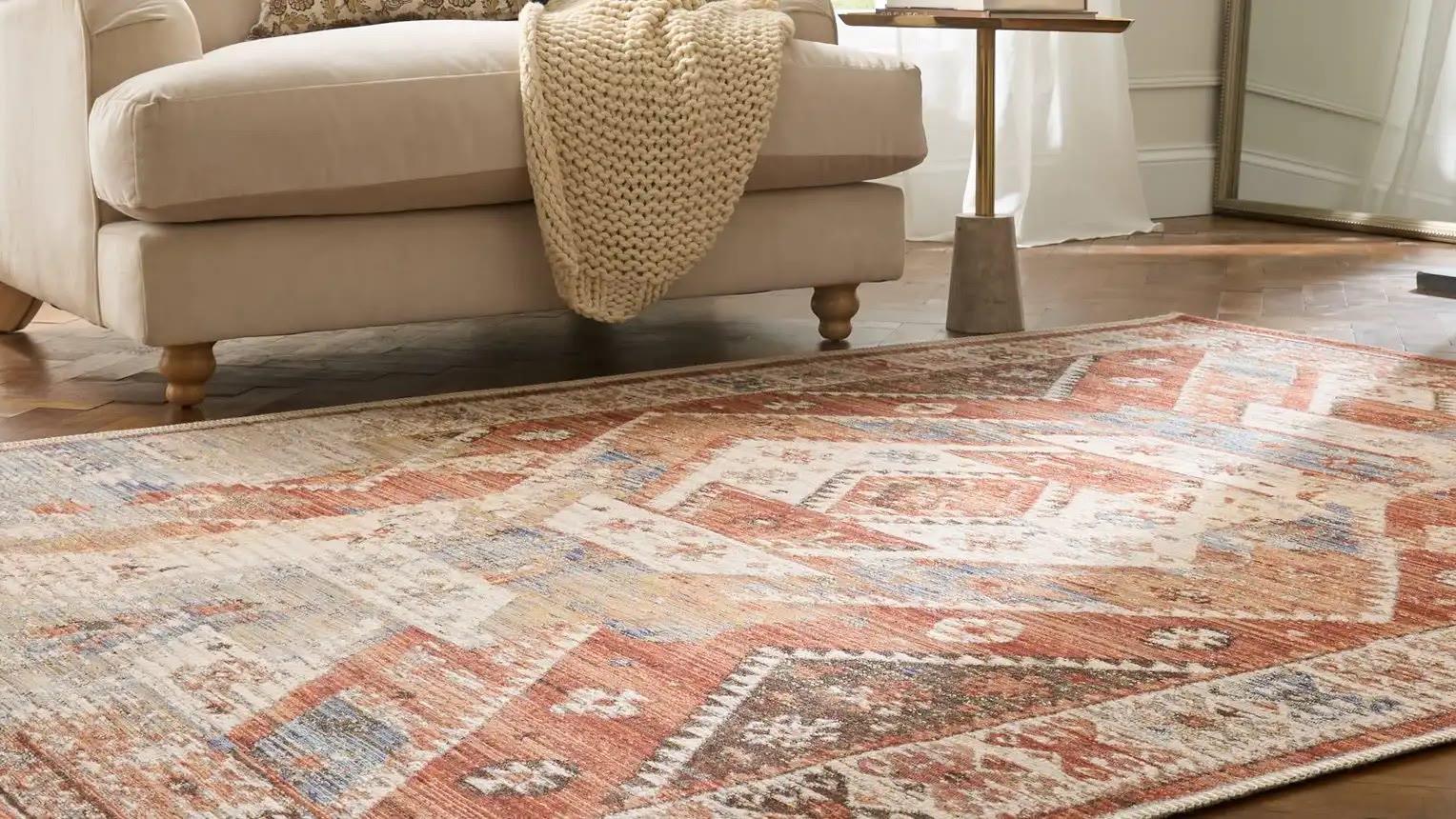 A Think Rugs terracotta medallion rug on parquet, under a cream armchair and side table