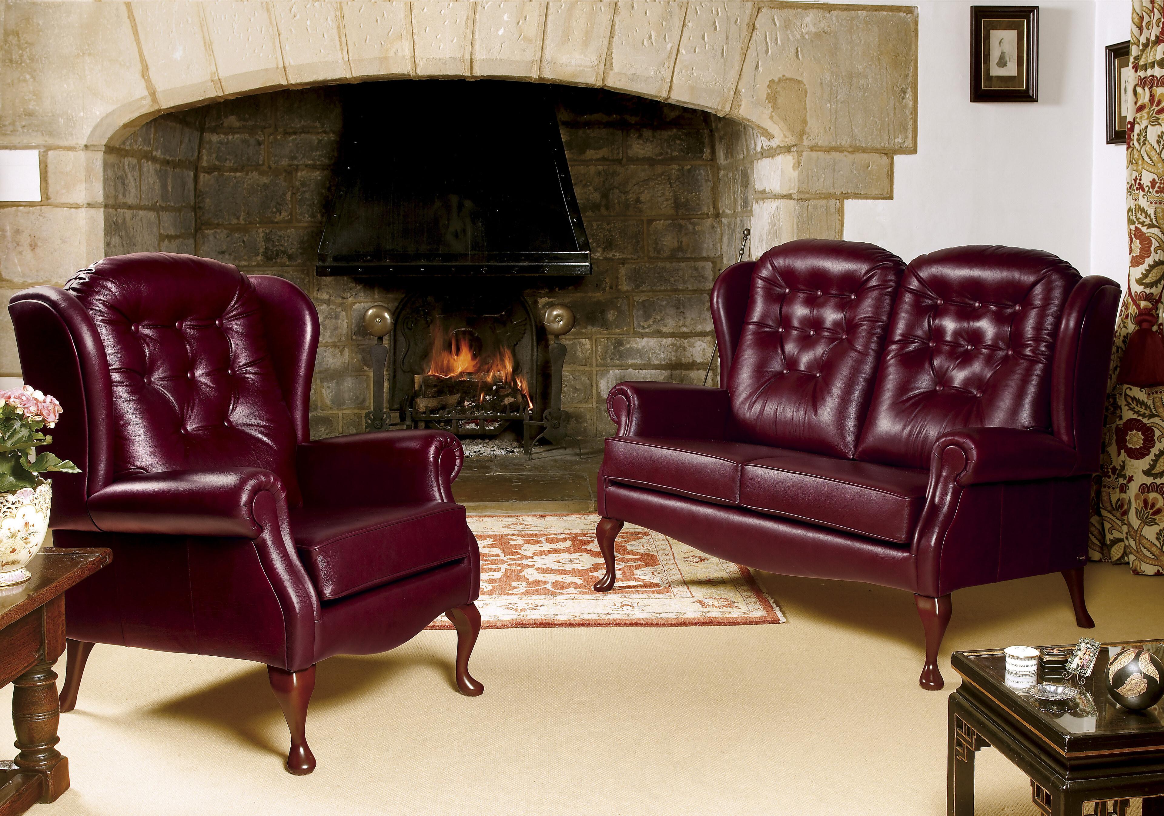 A Sherborne Lynton Fireside chair in oxblood leather, beside a stone inglenook fireplace with a lit fire
