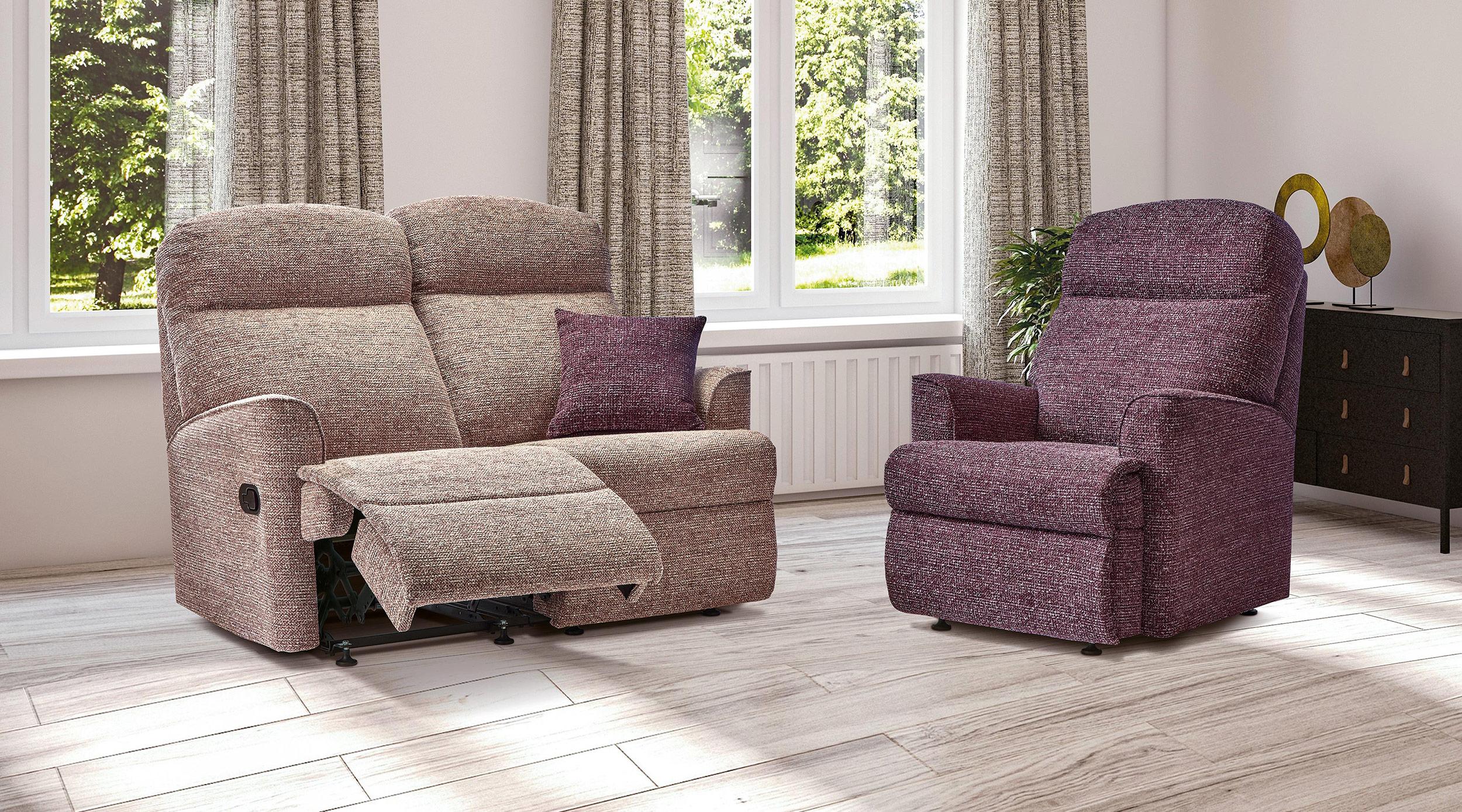An oatmeal Sherborne reclining sofa with its footrest raised, beside a plum recliner armchair in a bright, light-floored room.
