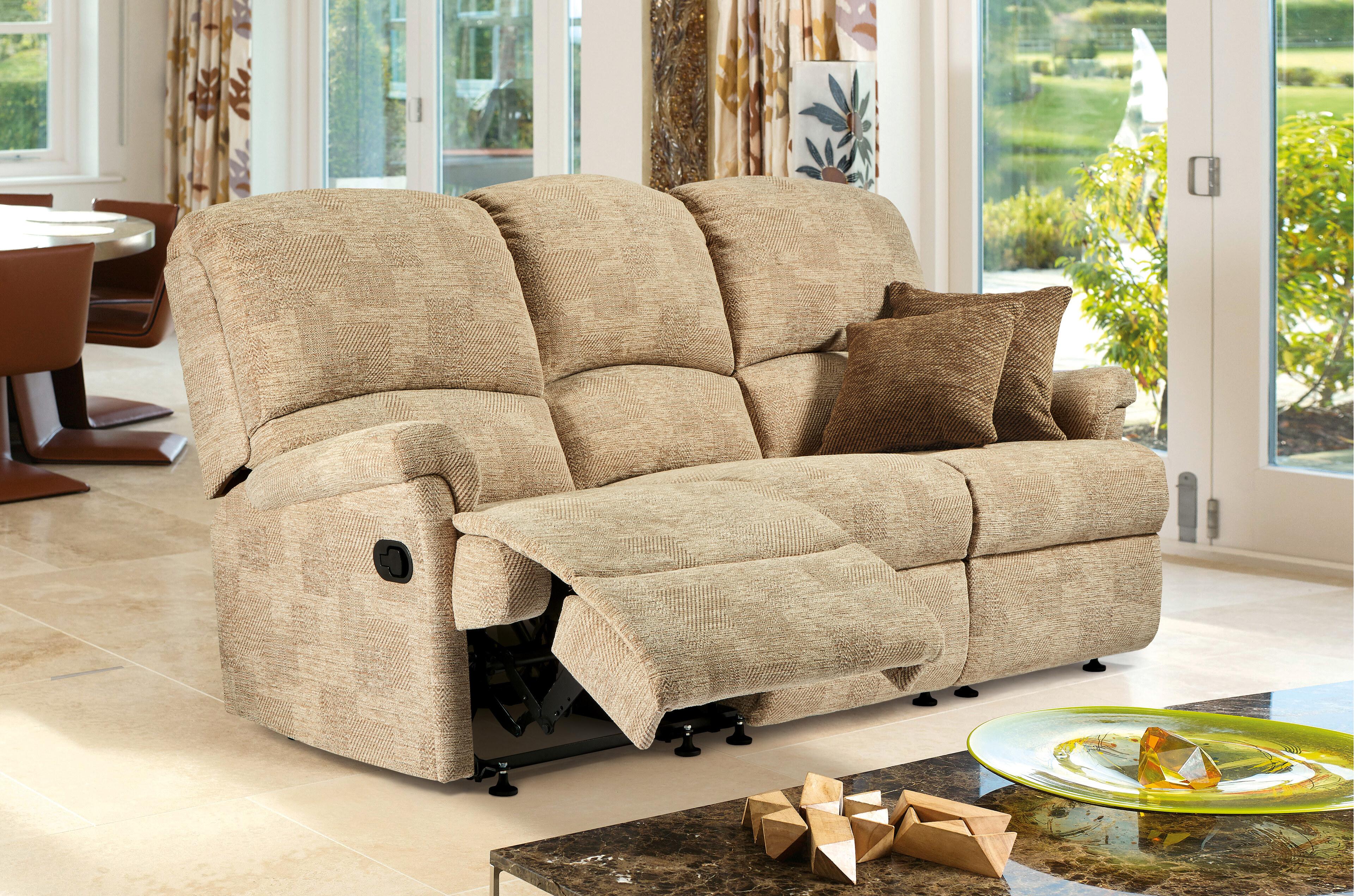 A Sherborne Nevada reclining three-seater sofa in oatmeal fabric, its near seat reclined with the footrest raised, in a bright room opening onto a garden.