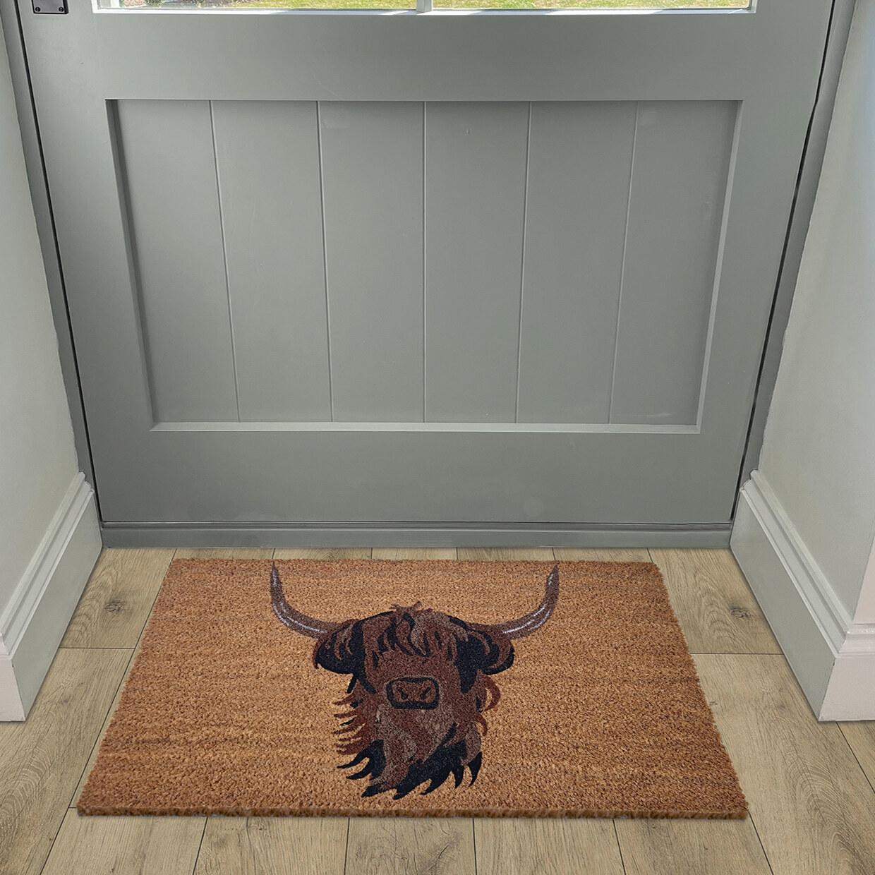 A natural coir doormat laid inside a sage-green front door.