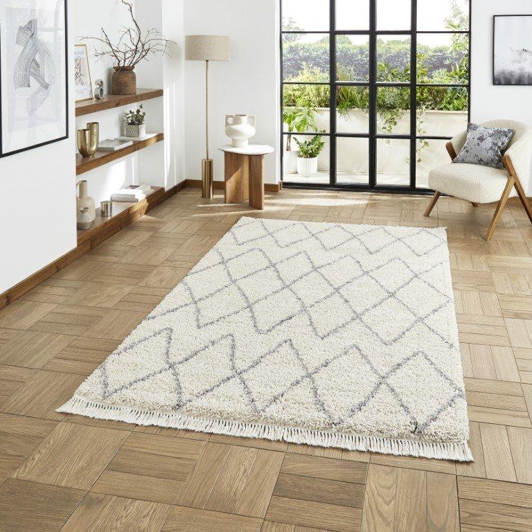 A cream and grey patterned Berber rug on a herringbone wood floor.